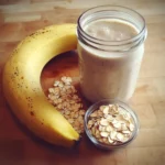 Creamy banana oatmeal smoothie with slices of fresh banana and rolled oats on a wooden surface. Perfect for healthy breakfast or snack options with natural ingredients and nutritious benefits.