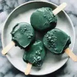 Vegan matcha green tea popsicles with a smooth, icy texture topped with a sprinkle of matcha powder on a white plate against a marble background.