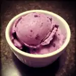 Creamy blueberry ice cream scoop in a white bowl on a dark surface, highlighting fresh and delicious homemade frozen dessert.