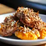 Savory meatloaf with oats and herbs served with creamy mashed sweet potatoes on a white plate.