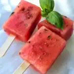 Juicy watermelon popsicles with fresh basil leaves, summer frozen treats, flavorful fruit ice lolly, healthy summer snack, refreshing watermelon ice treat for kids and adults.