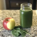 Fresh green smoothie in a glass jar with an apple and spinach on a granite countertop. Healthy vegan breakfast drink with leafy greens and fruit nutrition. Ideal for detox and wellness routines.
