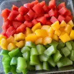 Sliced colorful bell peppers in red, yellow, and green arranged in a glass dish for fresh, healthy pet treats.