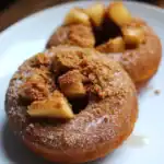 Sweet cinnamon apple cider donuts topped with crushed cookie crumbs and fresh apple pieces, served on a white plate for a delicious treat.