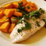 Golden baked salmon fillet topped with fresh herbs and served with roasted sweet potatoes and herbs on a white plate. Healthy, protein-rich seafood meal for dinner or lunch.