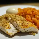 Quinoa-crusted fish fillet with roasted sweet potatoes and a boiled egg on a white plate, showcasing a healthy, protein-rich meal. Perfect for nutritious diets and family dinners.