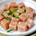 Cubed raw chicken breast topped with chopped green onions on a white plate, ready for cooking or seasoning. Perfect for healthy chicken recipes and meal prep.