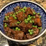 Hearty beef stew with tender beef chunks, bright green peas, and rich gravy served in an elegant blue and white bowl. Perfect comfort food for cold days or family dinners.