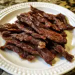 Succulent grilled beef jerky showing well-seasoned, savory strips on a white plate, perfect for snack or gourmet dish, highlighting Waggy Chef's flavorful homemade beef jerky.
