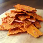 Crispy homemade beef jerky on a wooden cutting board, seasoned with spices and herbs, perfect for healthy snacking.