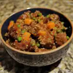 Savory beef stew with tender chunks of beef, carrots, peas, and quinoa in a rich, flavorful sauce served in a black bowl. Perfect for comfort food and healthy eating.