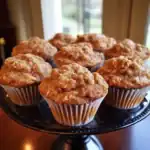 Golden brown homemade apple cinnamon muffins with crumbly topping on a black cake stand, perfect for breakfast or snack.