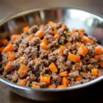 Ground beef and diced carrots in a stainless steel mixing bowl, ready for cooking or meal prep. Perfect example of healthy, homemade pet food or dog food recipe.