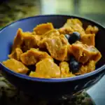 Golden sweet potato dog treats in a black bowl with blueberries, healthy homemade dog snack, pet feeding, nutritious dog treats, Waggy Chef.