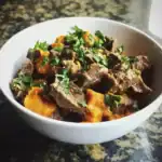 Savory beef stew with sweet potatoes and fresh herbs in a white bowl, healthy dog food made with Waggy Chef ingredients.